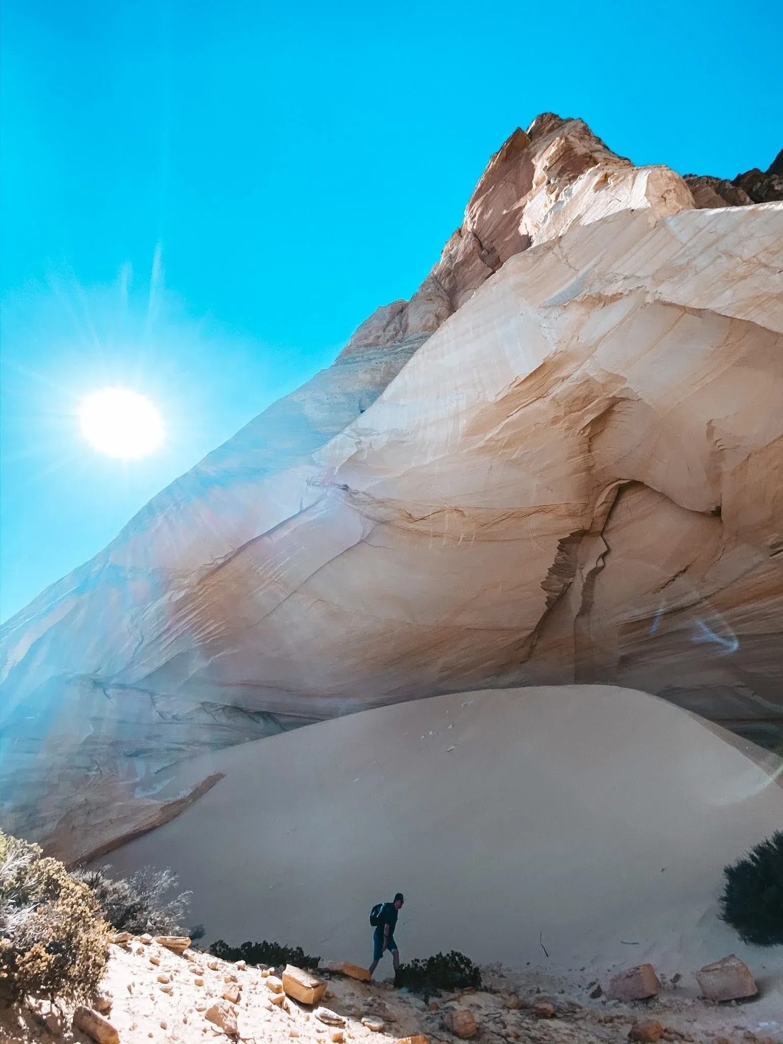 Sunlit sandstone arch in a desert, with a person standing beneath it under a bright blue sky