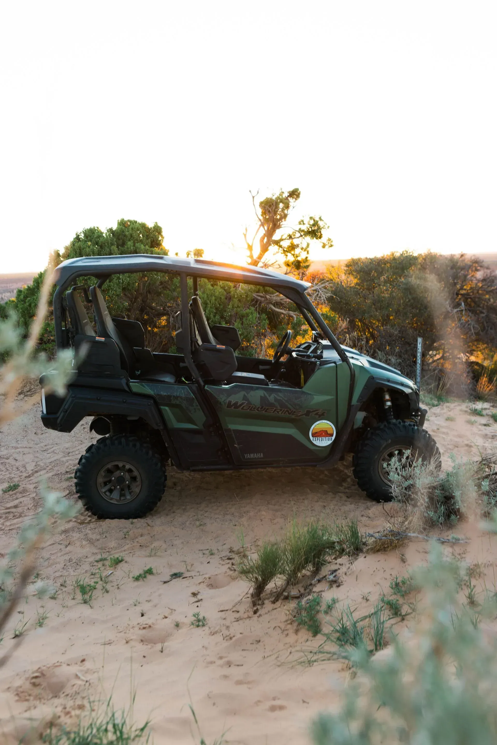 Green off-road side-by-side parked on sandy terrain at sunset