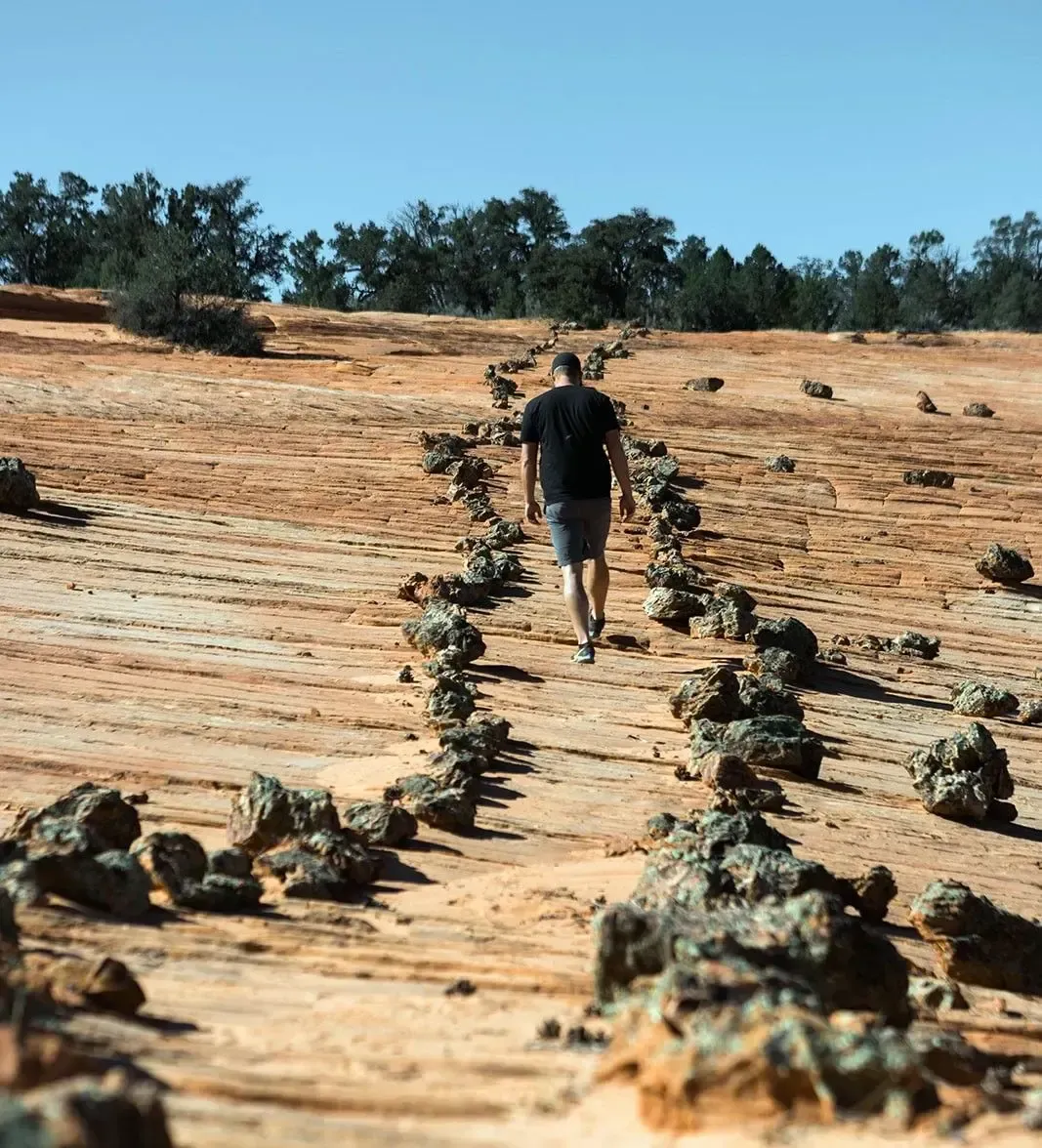 A man is walking down a dirt path in the desert.