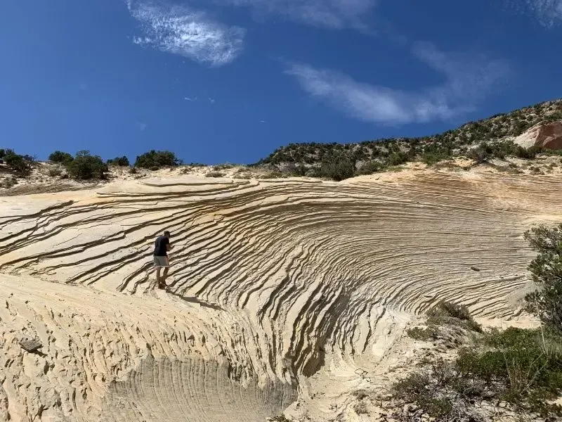 Person standing on weathered sandstone formation under blue sky.