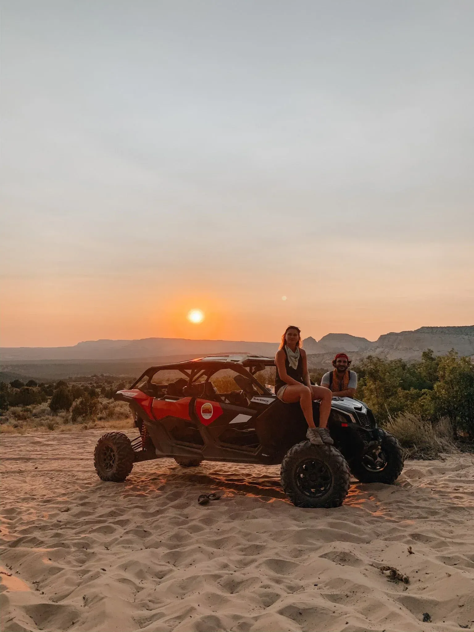 Two people riding an off-road buggy on sandy dunes at sunset