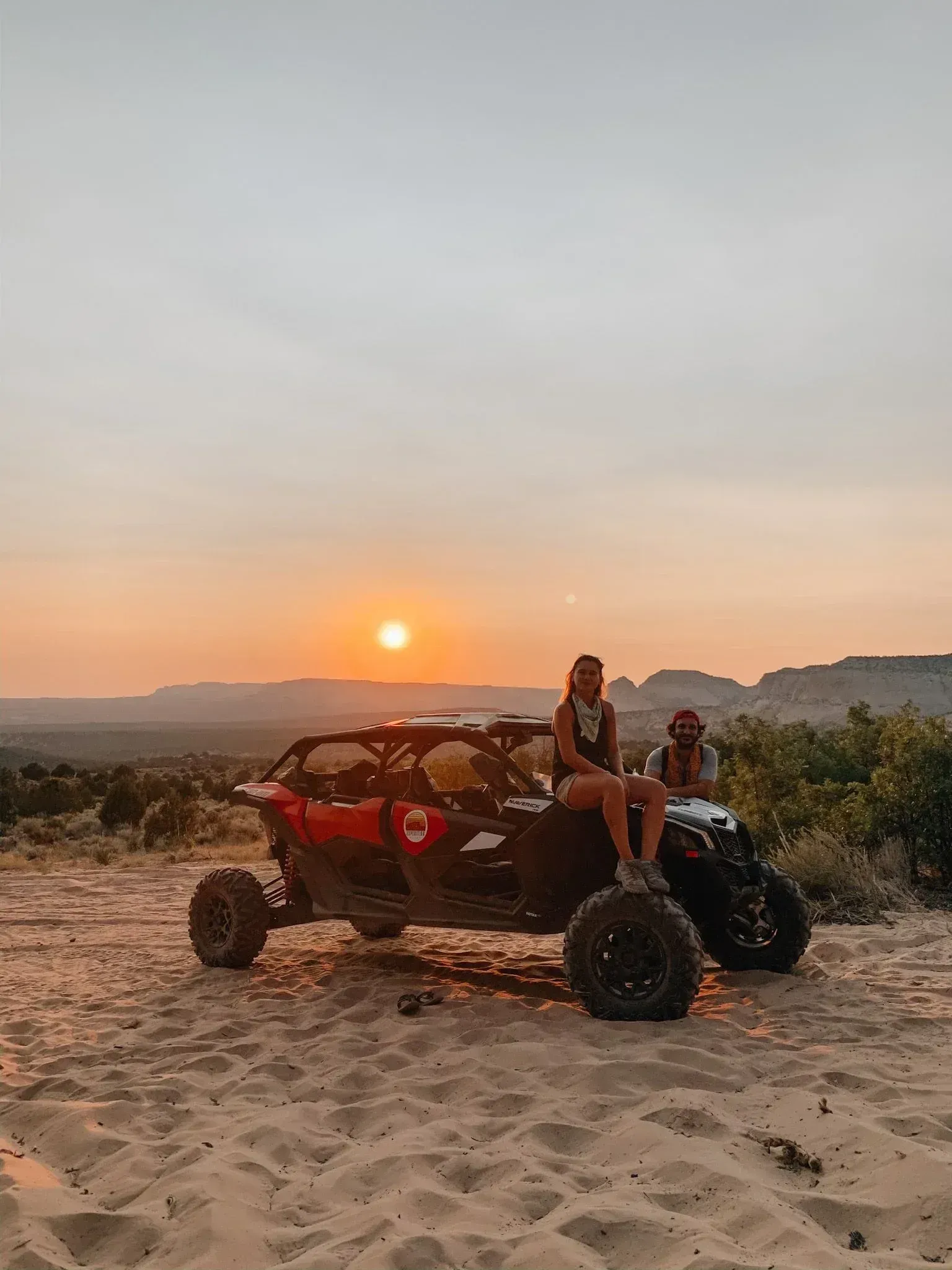 Two people on a red dune buggy at sunset in a sandy desert