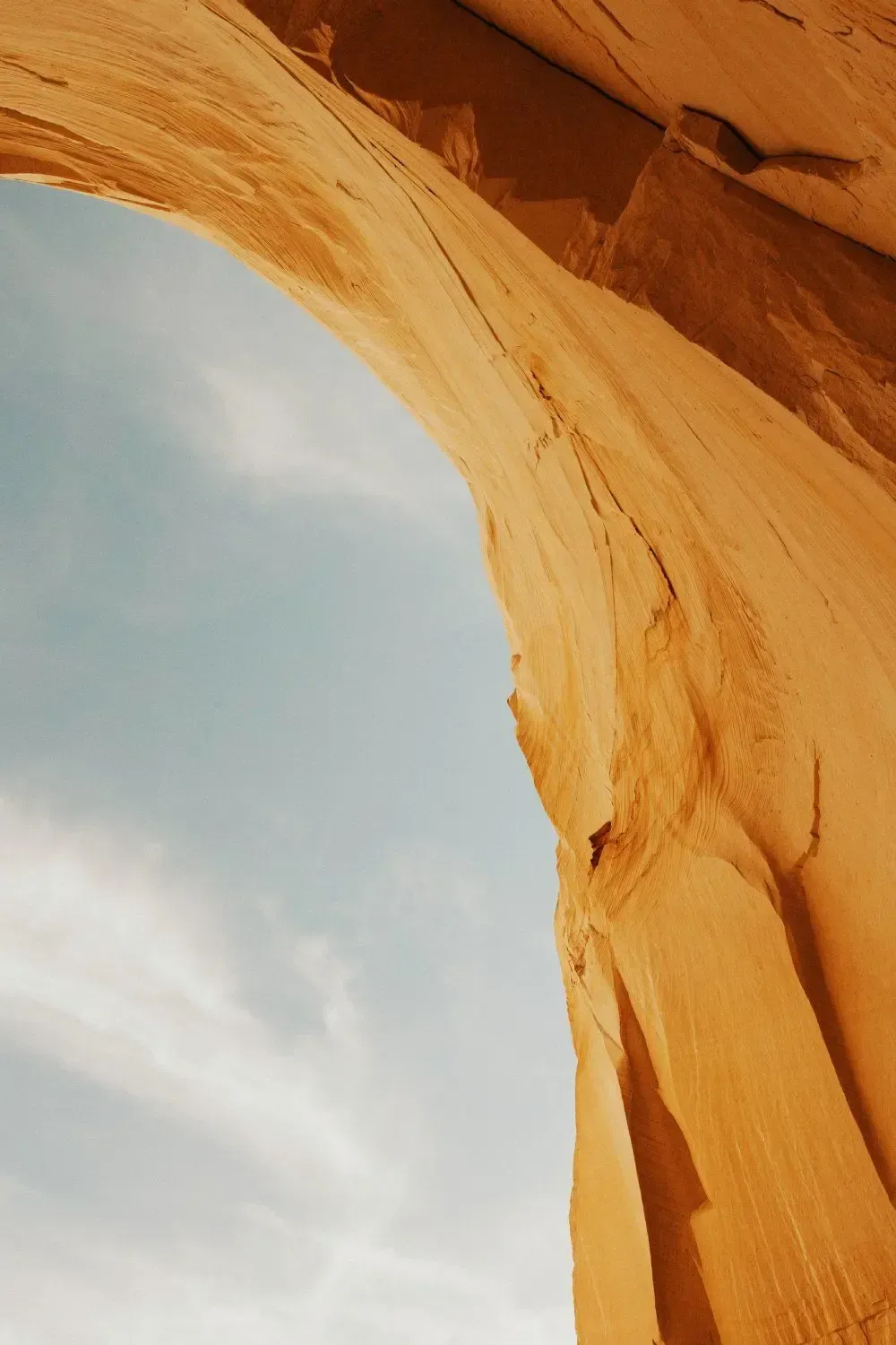 Orange sandstone arch framing a blue sky and wispy clouds