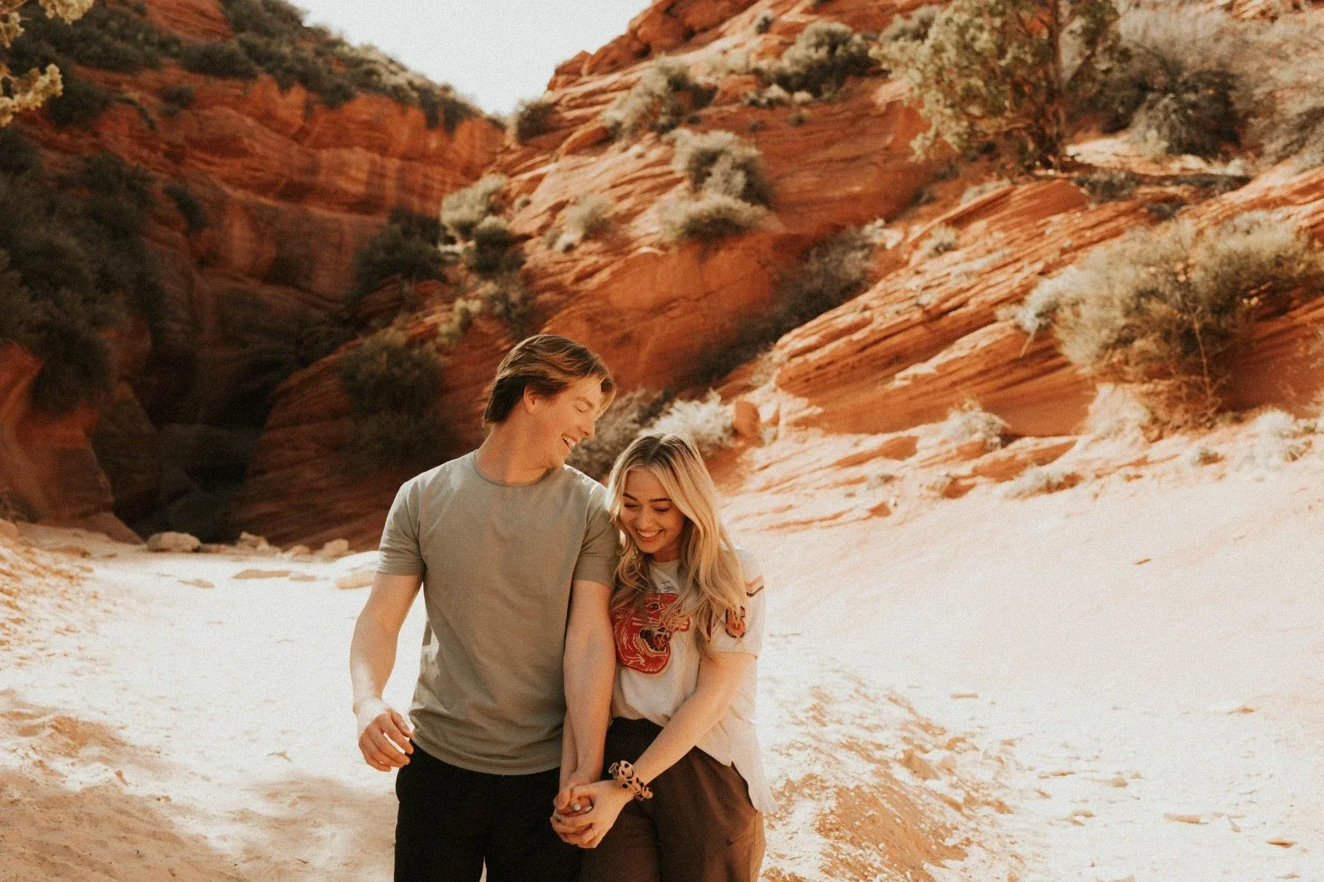 Couple walking together in a sunlit red-rock canyon, smiling and looking at each other