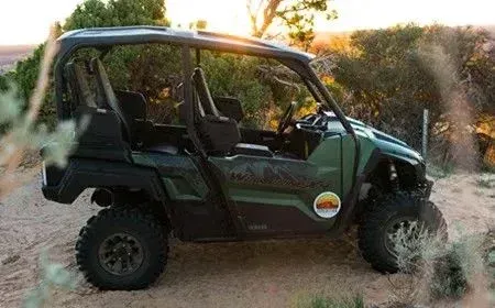 Green off-road vehicle driving through dusty terrain at sunset