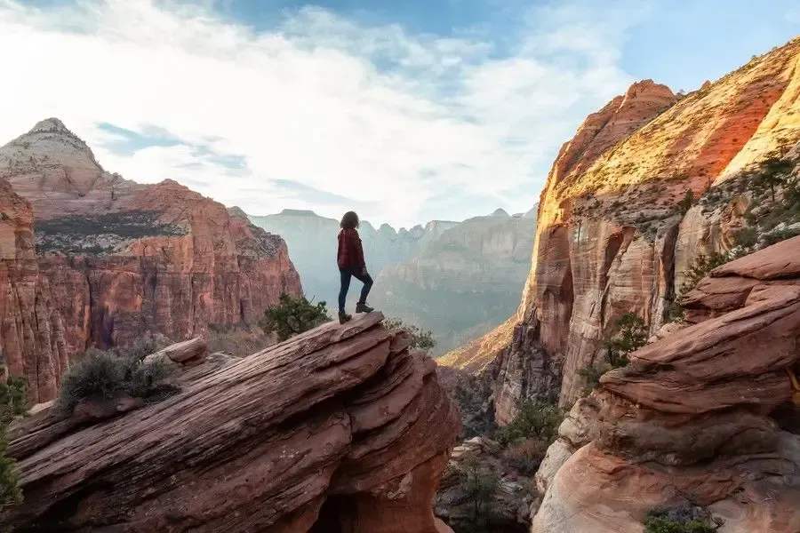 A person is standing on top of a rocky cliff overlooking a canyon.