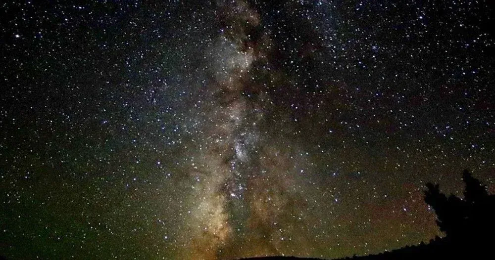 Milky Way arcing across a star-filled night sky above dark hills and tree silhouettes
