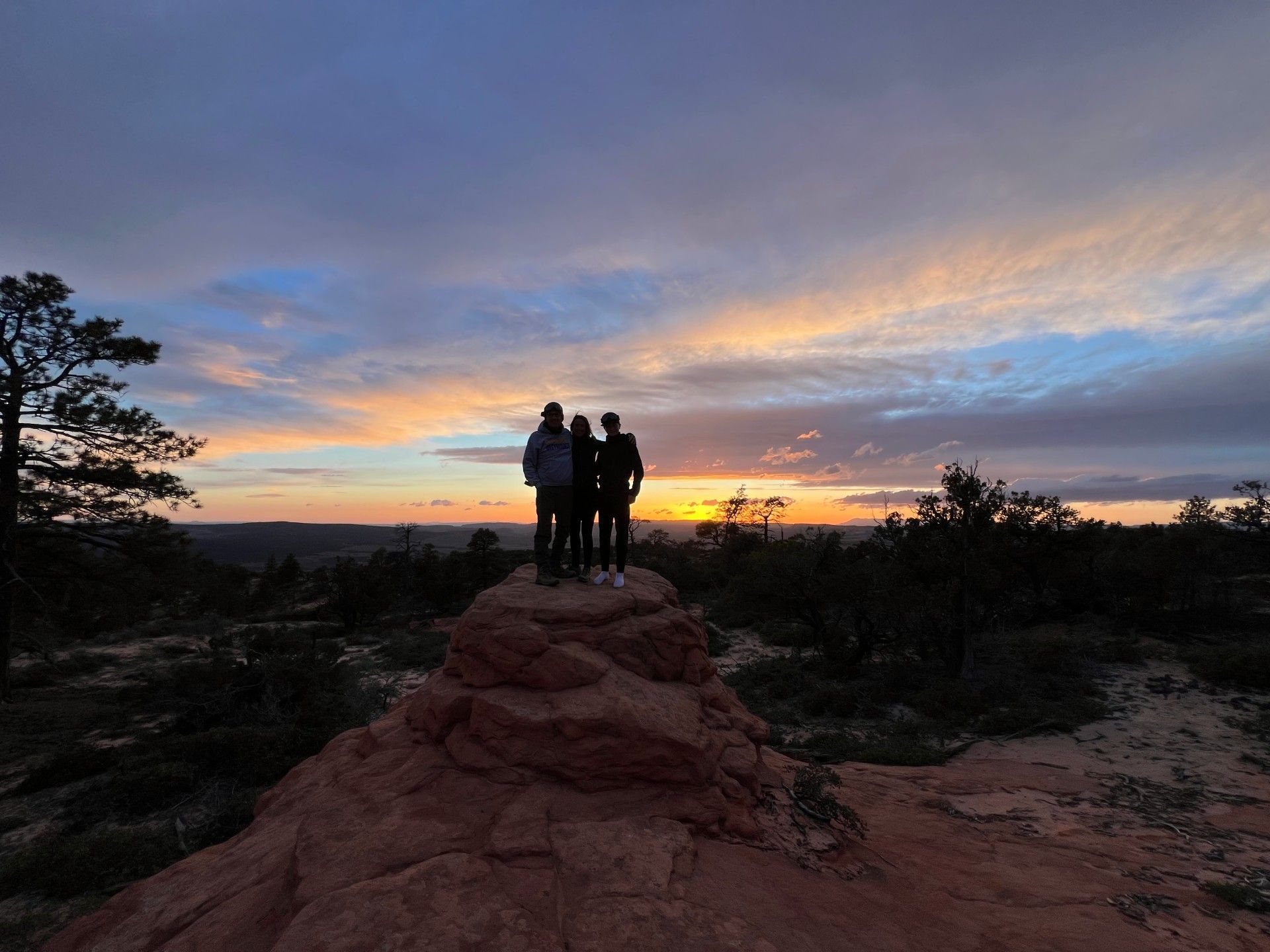 Silhouetted group on a red rock at sunset with a colorful cloudy sky and desert shrubs