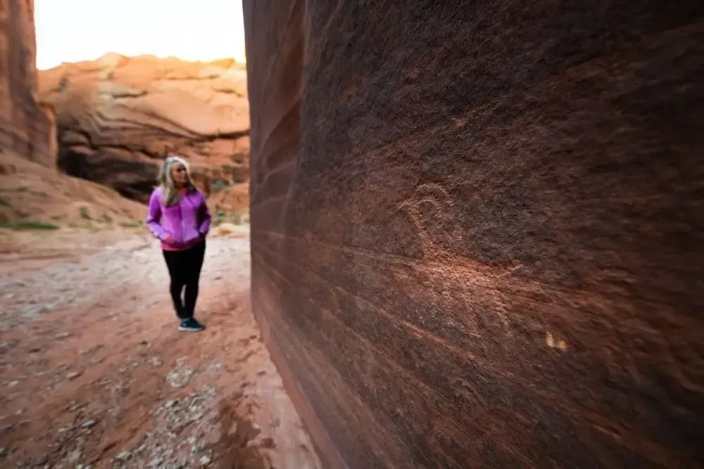 Person in a pink jacket walks through a narrow red sandstone canyon.