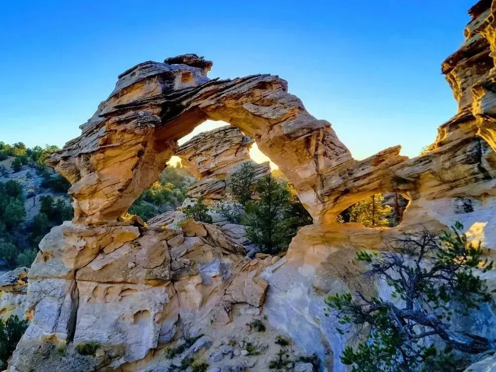 Natural sandstone arch formation in a rocky desert landscape at sunset.