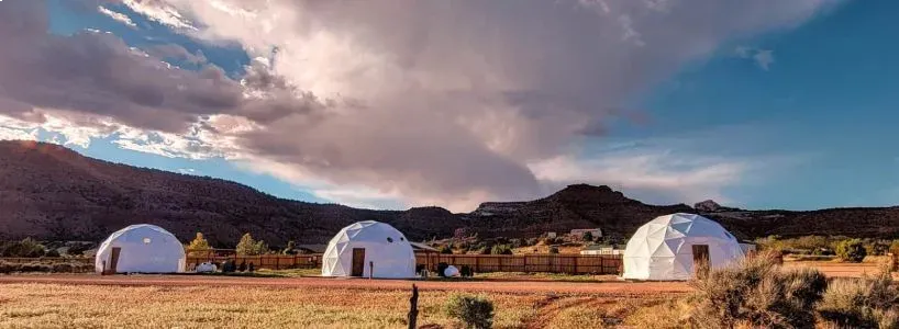 A row of white tents in a field with mountains in the background.