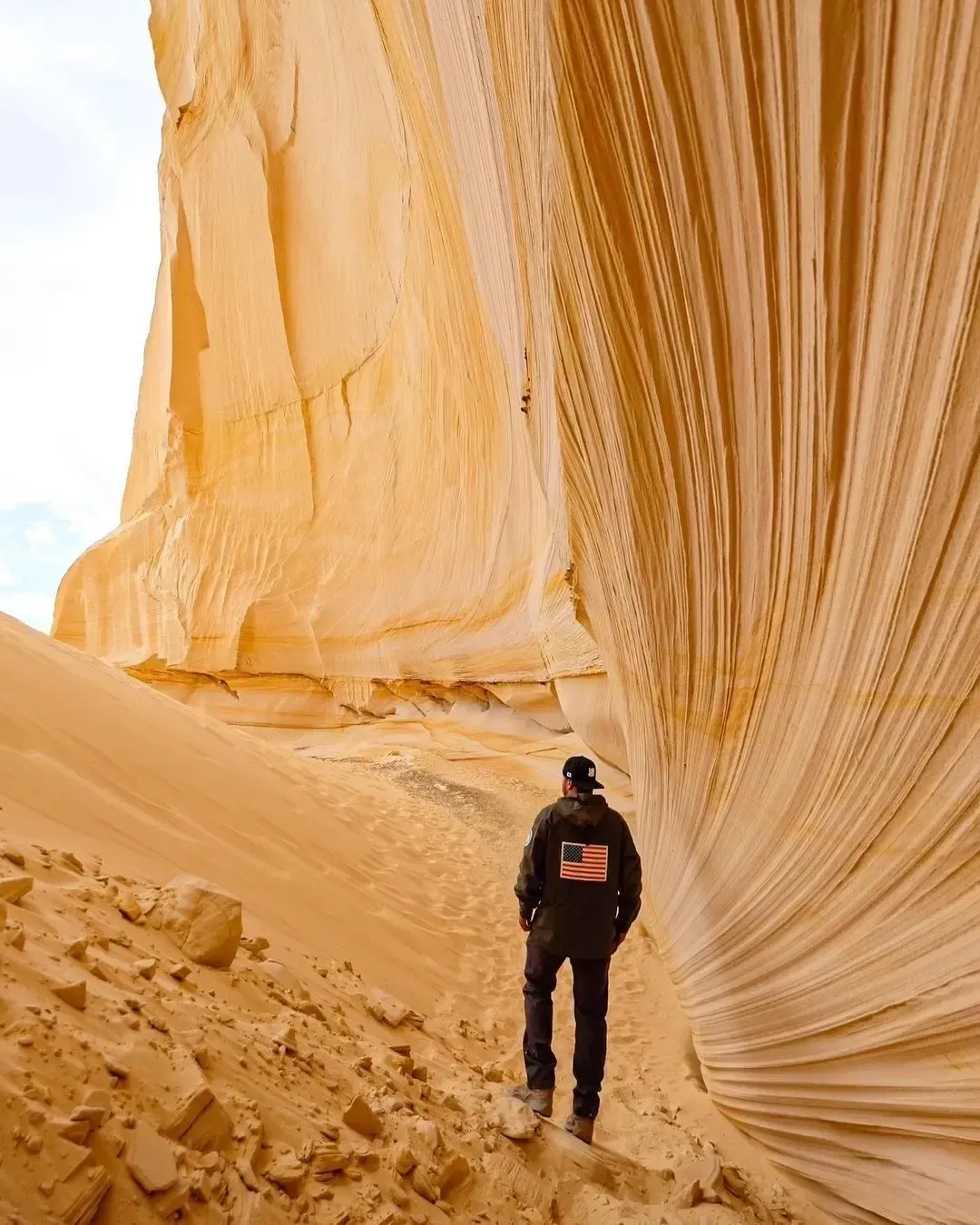 Person standing in a golden sandstone canyon with wavy rock walls and sandy ground