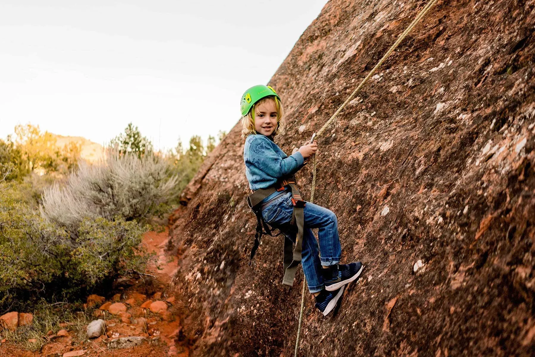 A young boy is climbing a rock wall with a rope.