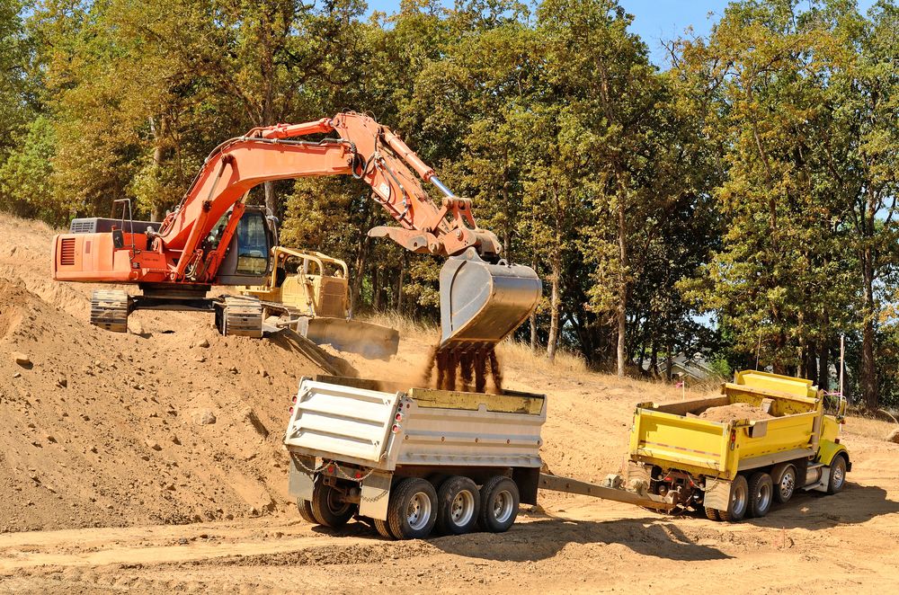 An Excavator Is Loading Dirt Into A Dump Truck — Northstar Excavations In Byron Bay, NSW
