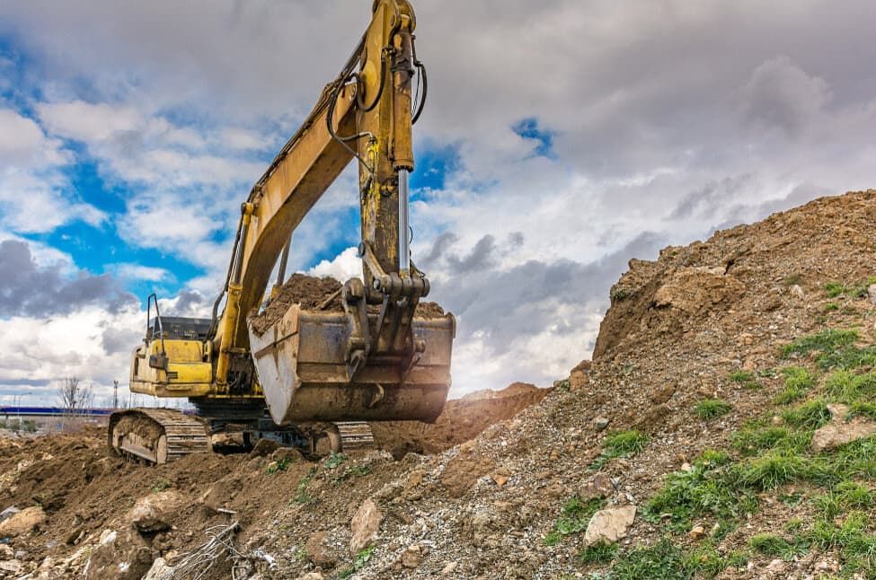 A Yellow Excavator Is Moving Dirt On A Hill — Northstar Excavations In Alstonville, NSW