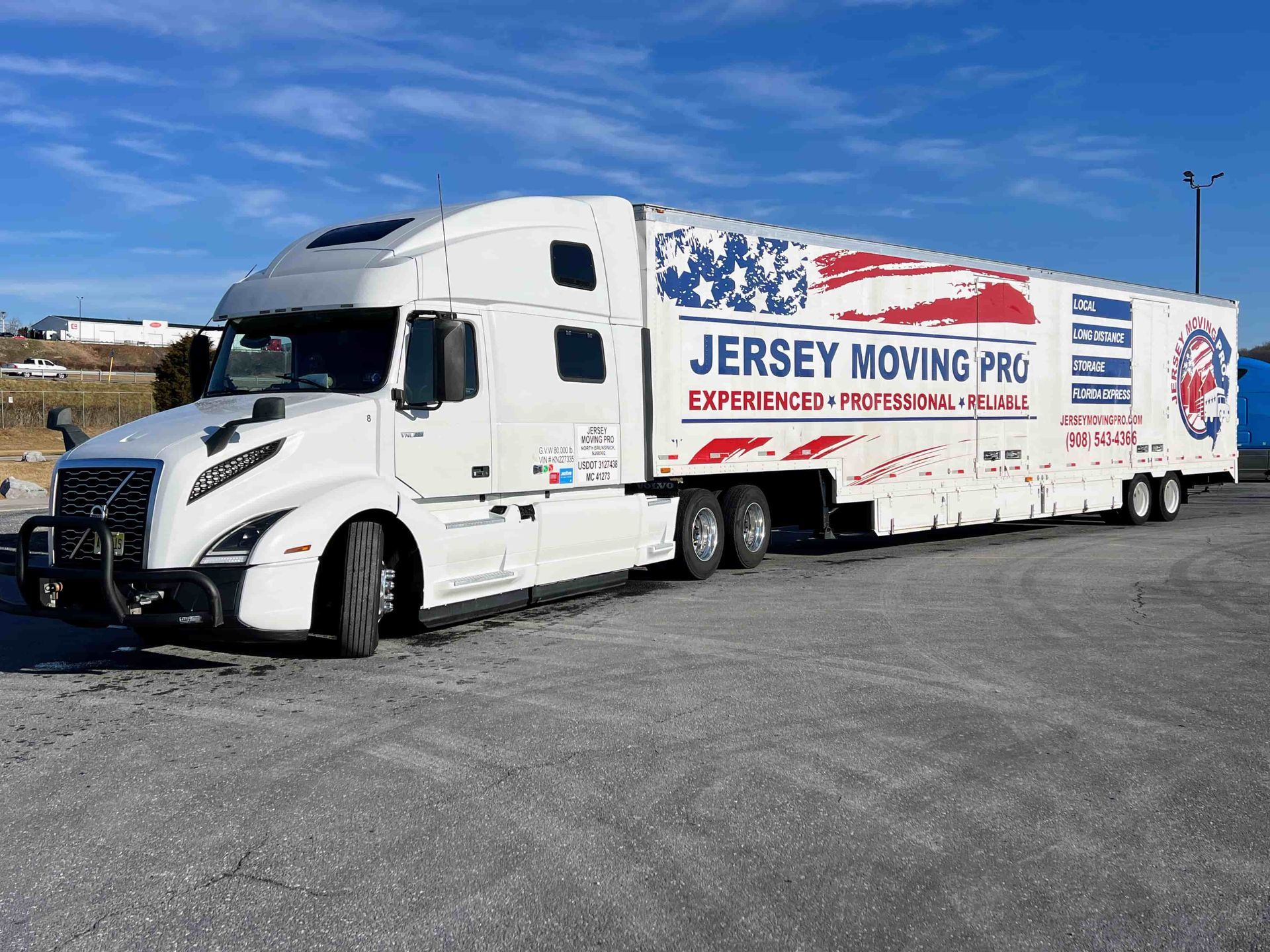 A white Jersey Moving Pro semi-truck parked in an outdoor gravel lot under a clear blue sky.
