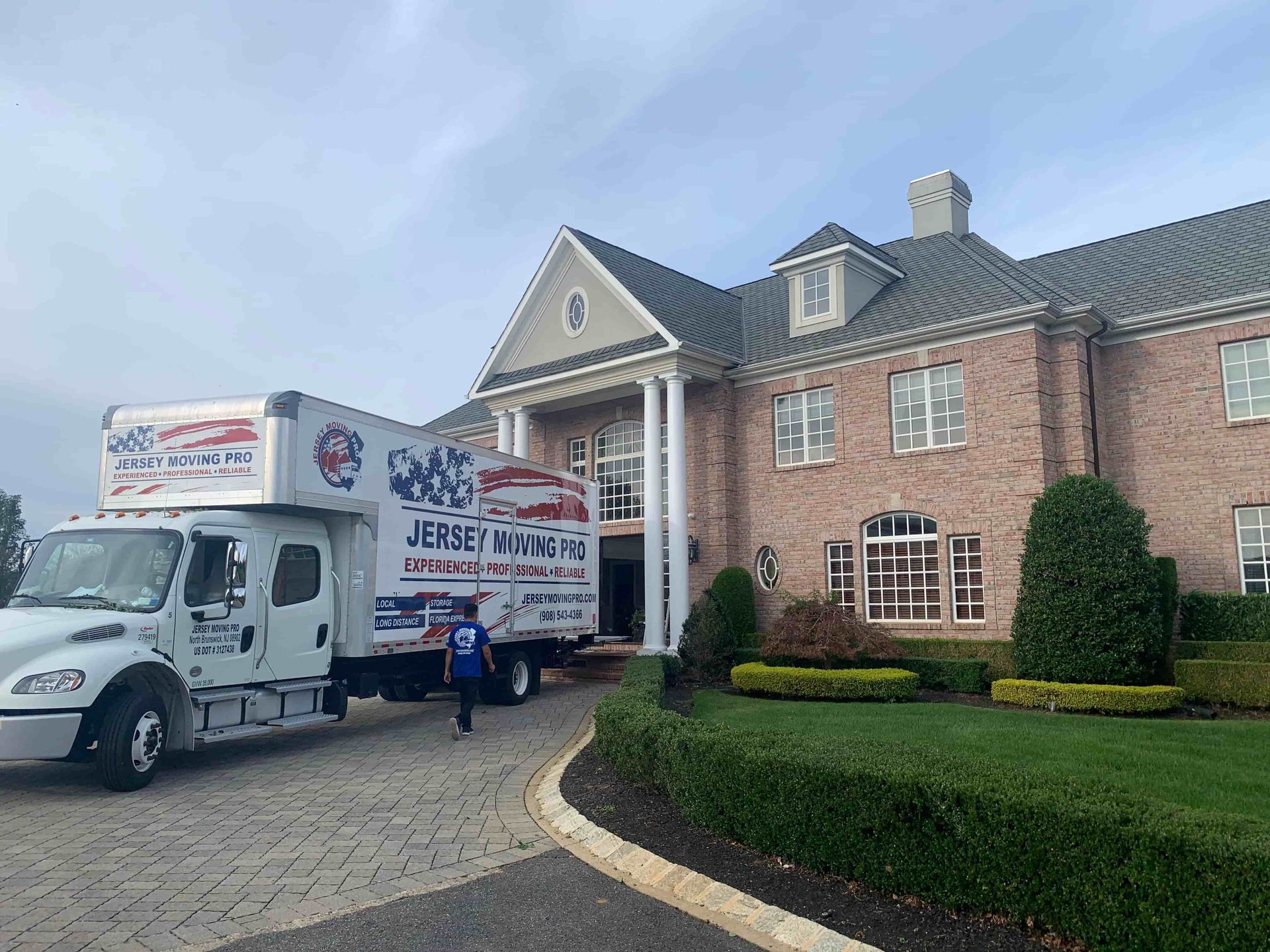 Moving truck parked in front of a large house with columns. A person walks toward the truck.