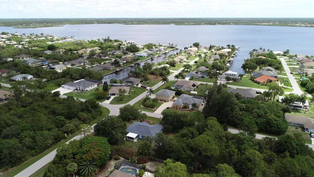 An aerial view of a residential neighborhood with houses nestled among green trees, bordering a large lake and canal.