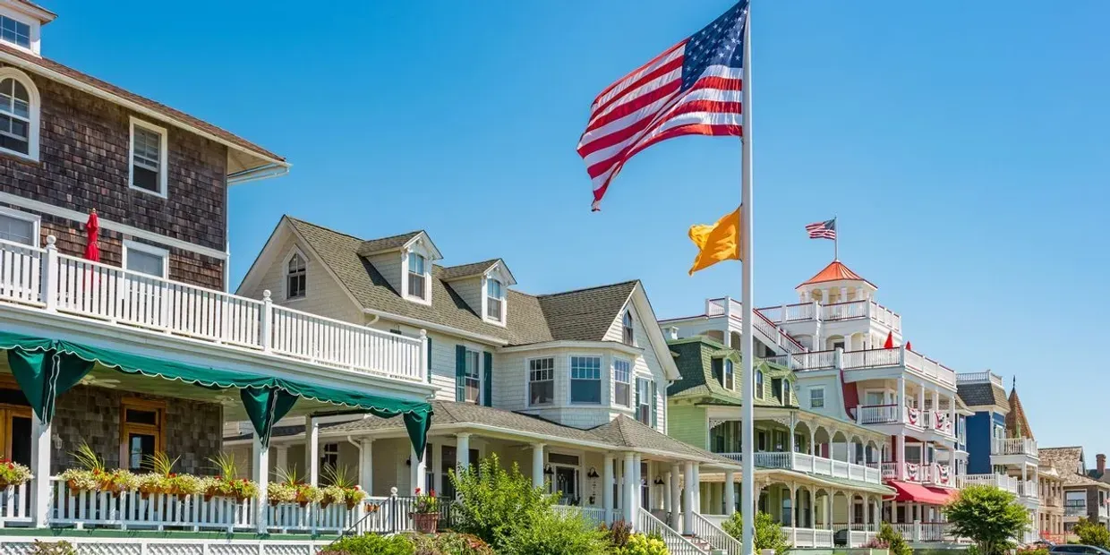 Row of coastal Victorian homes with porches, flying a large American flag under a clear blue sky.