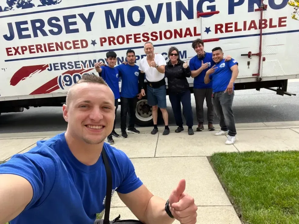 Jersey Moving Pro team poses with a truck. Smiling people give thumbs-up outside. Blue and white colors.