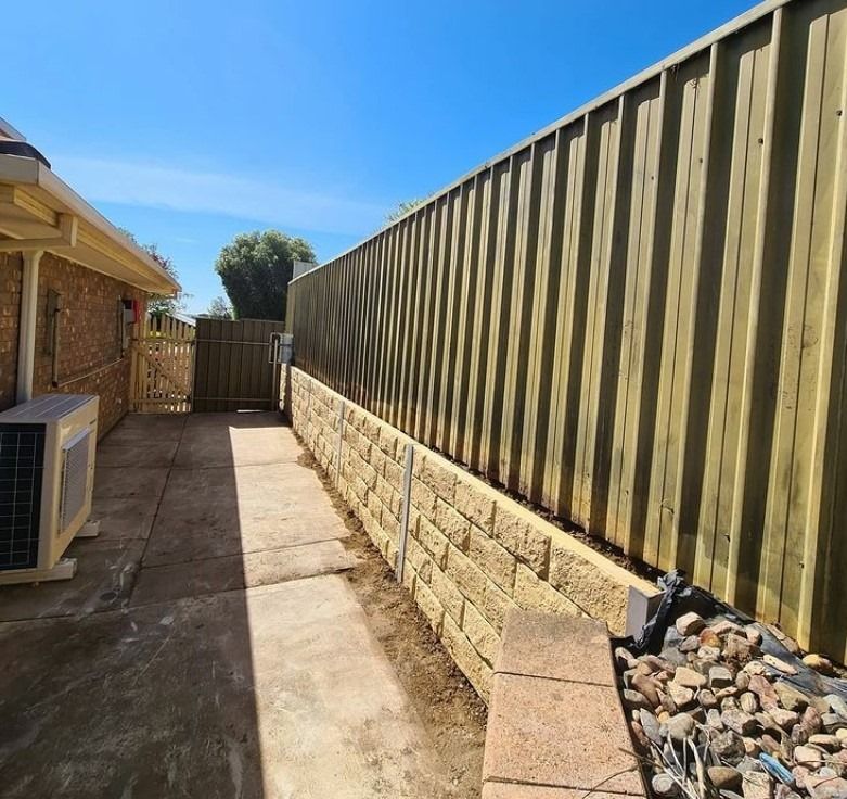 Narrow concrete path beside a timber fence and brick house under a bright blue sky