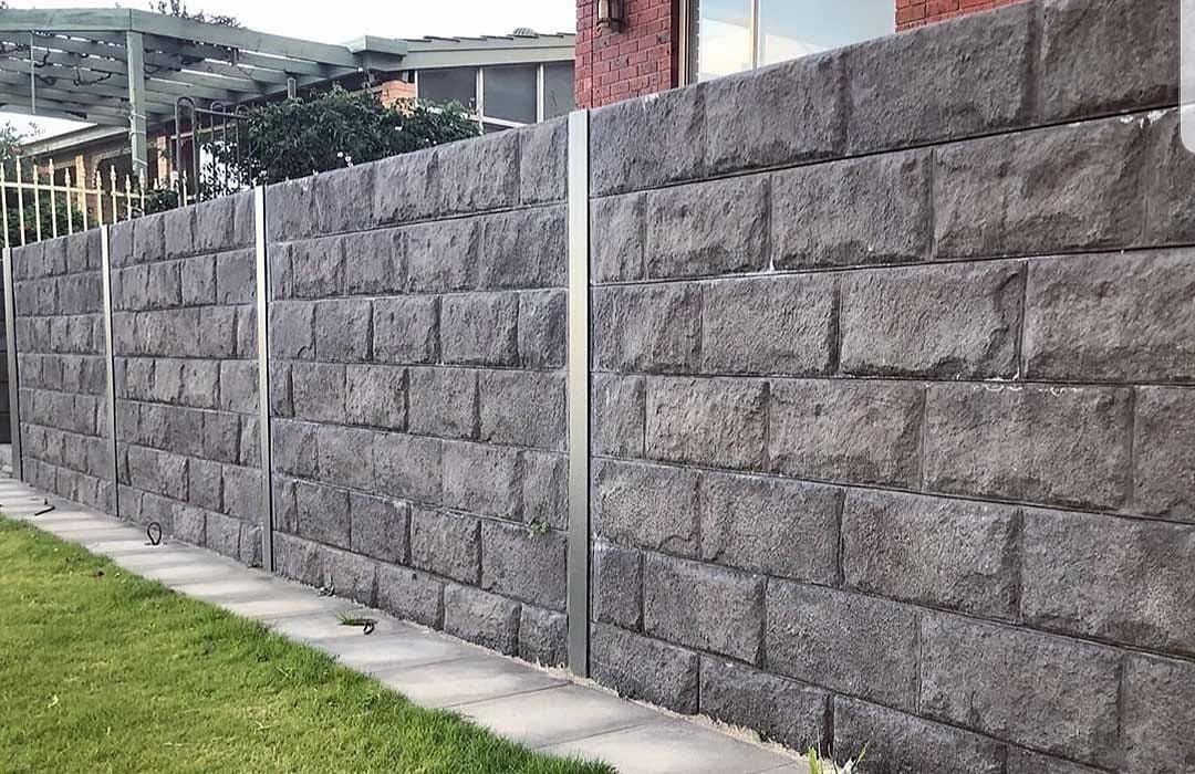 Gray stone retaining wall beside a grassy lawn and concrete walkway outdoors