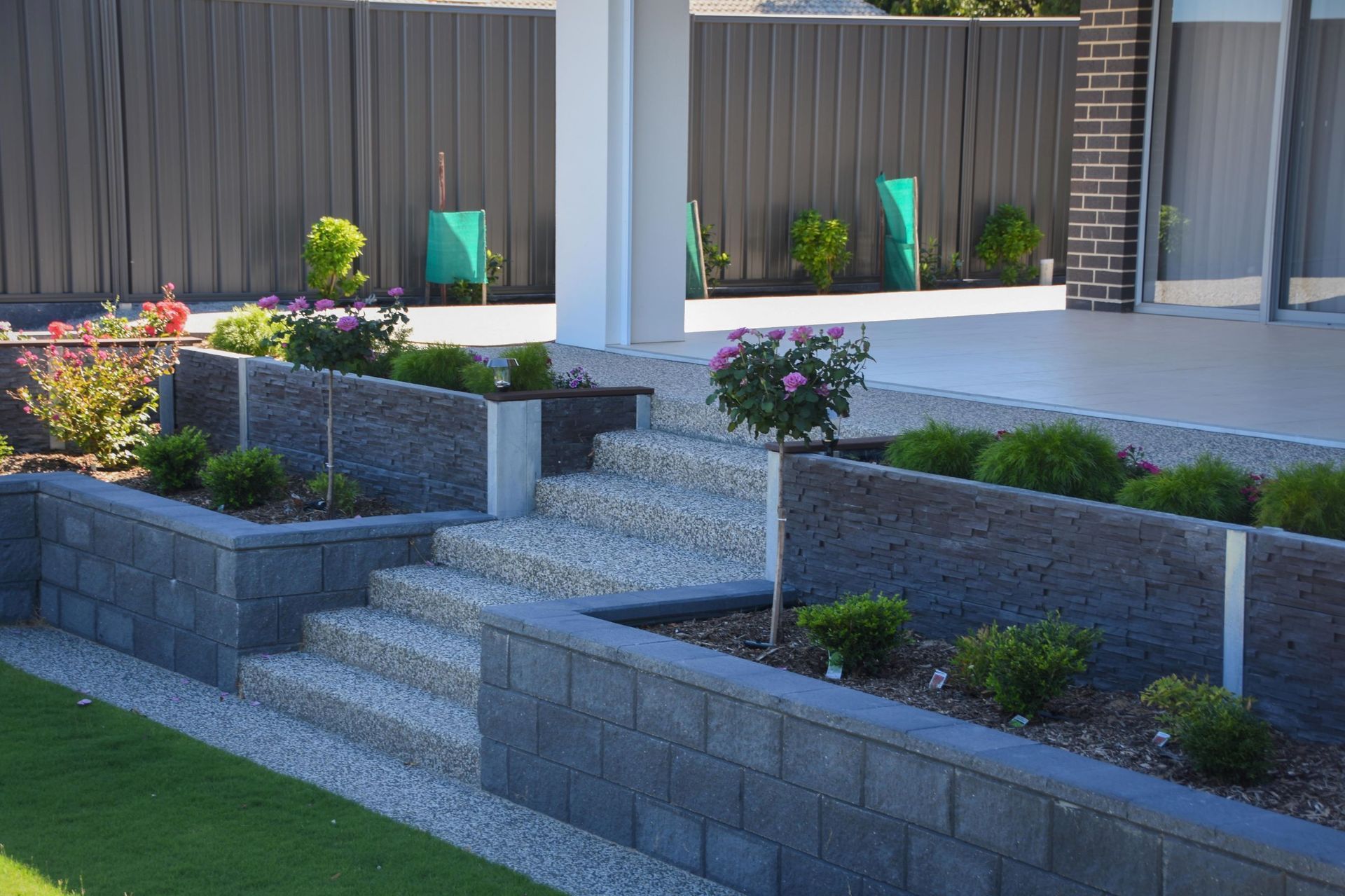 Modern front yard with stone steps, retaining walls, and landscaped flower beds by a driveway
