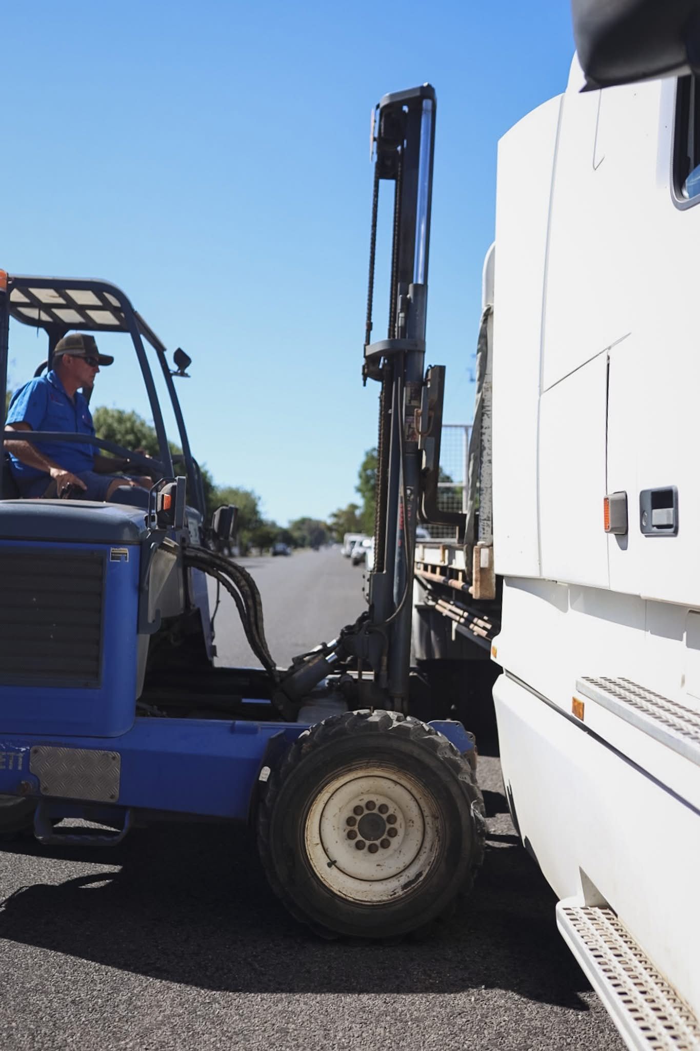 Blue forklift lifting white semi-truck on roadside under clear sky — Hunter Valley Bricks & Pavers in Scone, NSW