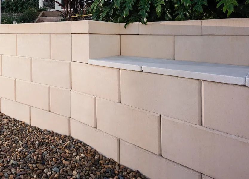 Tan Brick Retaining Wall With Gravel Base, Next to Green Foliage — Hunter Valley Bricks & Pavers in Scone, NSW