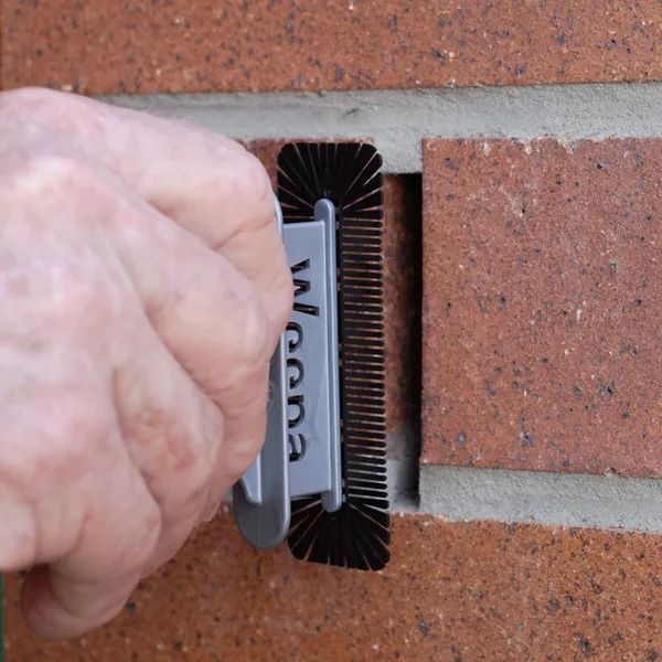 Hand Using a Cleaning Tool With Bristles to Clean the Mortar Between Bricks — Hunter Valley Bricks & Pavers in Scone, NSW