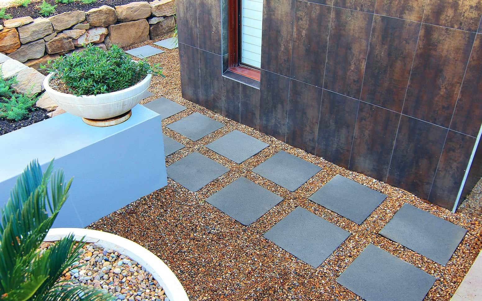 Stone path squares through gravel beside a modern building, with planters and rock wall— Hunter Valley Bricks & Pavers in Scone, NSW