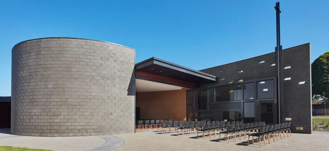 Modern Church Building With a Curved Stone Wall and Dark Rectangular Structure — Hunter Valley Bricks & Pavers in Scone, NSW