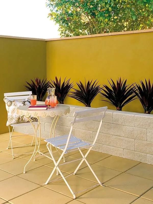 Outdoor Patio With a Table, Chairs, Plants in a Planter Against a Yellow Wall — Hunter Valley Bricks & Pavers in Scone, NSW