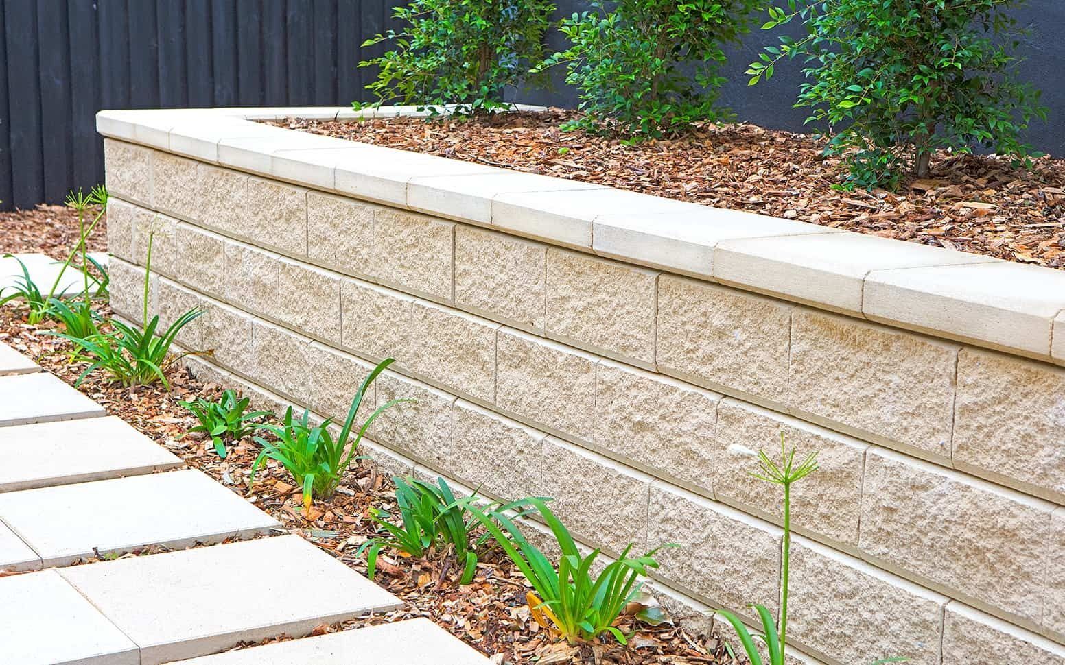 Beige Retaining Wall With Stone Pavers, Mulch, and Greenery — Hunter Valley Bricks & Pavers in Scone, NSW