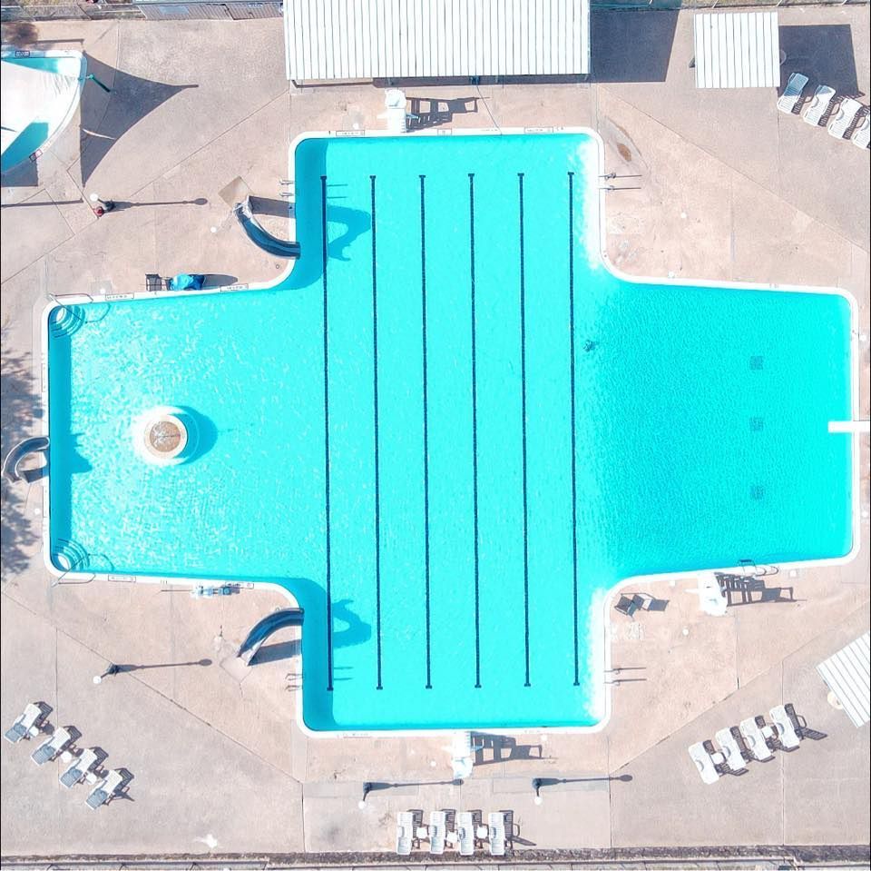 Aerial view of a bright turquoise swimming pool with lanes, surrounded by a concrete deck and lounge chairs.