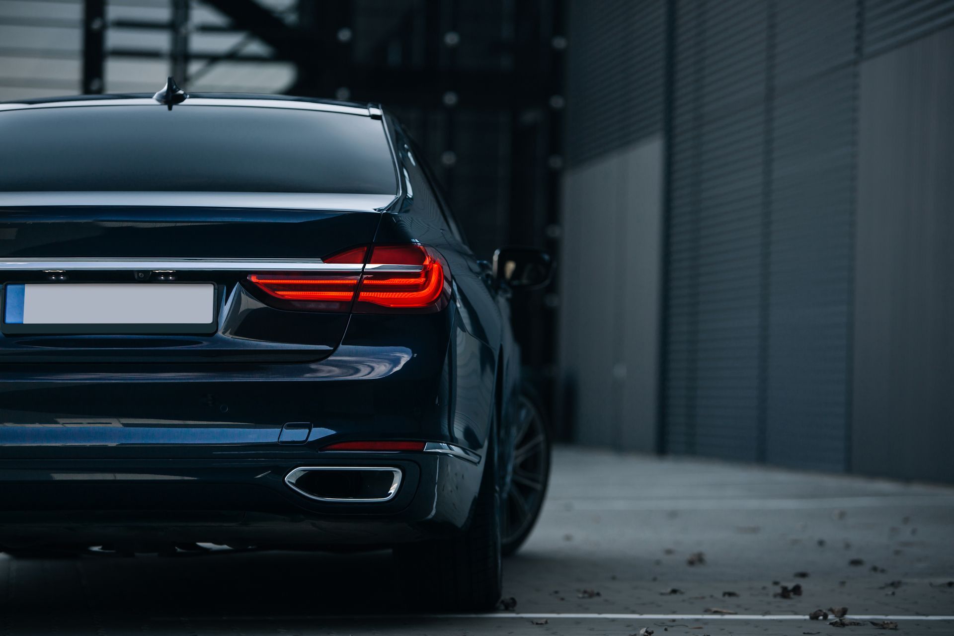 Black luxury sedan parked in a modern architectural space, with taillights illuminated.