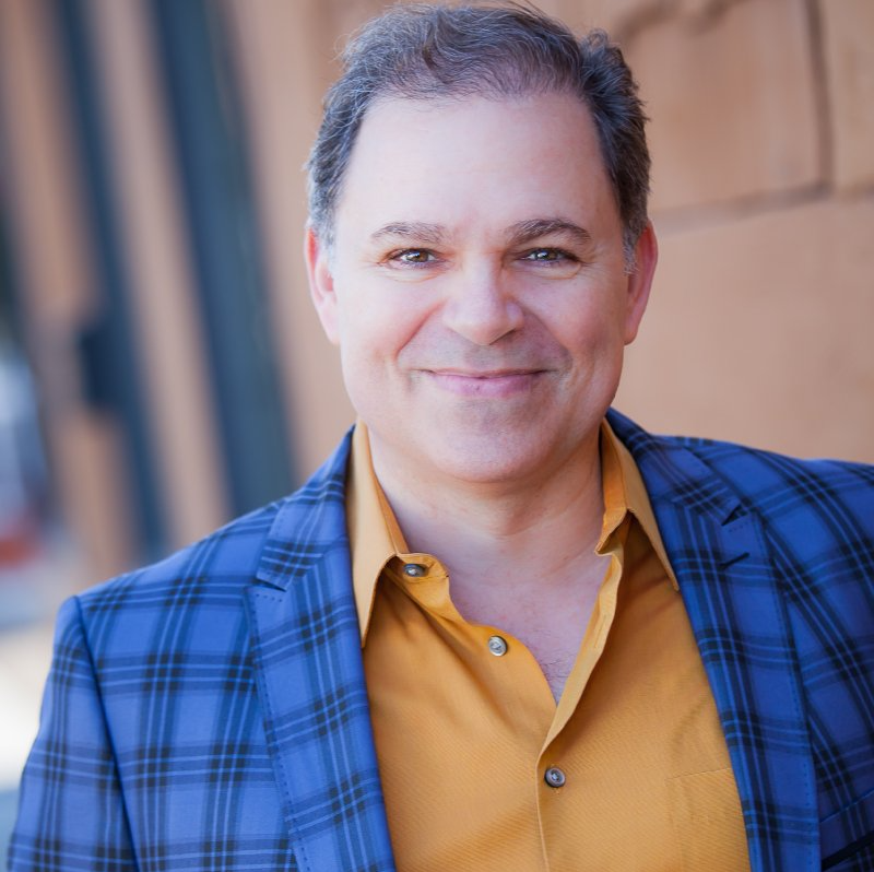 Phil, smiling, wearing blue checked suit jacket and gold shirt