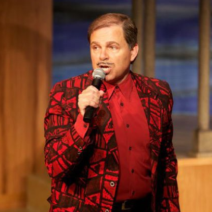 Phil in colorful jacket holding microphone and singing