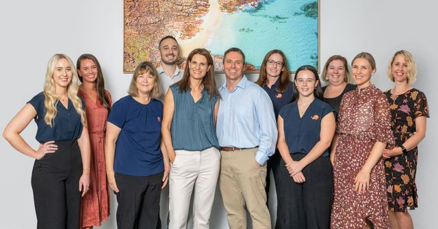 Group of nine people standing together indoors in front of a colorful world map mural