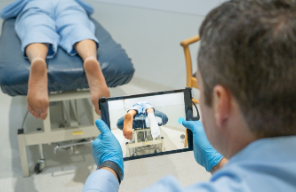 Physical therapist using a tablet to record a patient’s leg exercise on a treatment table