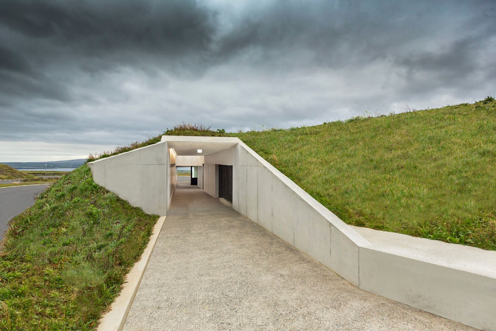 A tunnel leading to a building on top of a grassy hill.