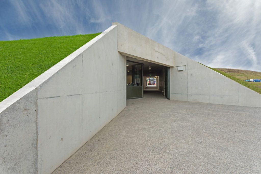 A concrete building with a grassy hill in the background.