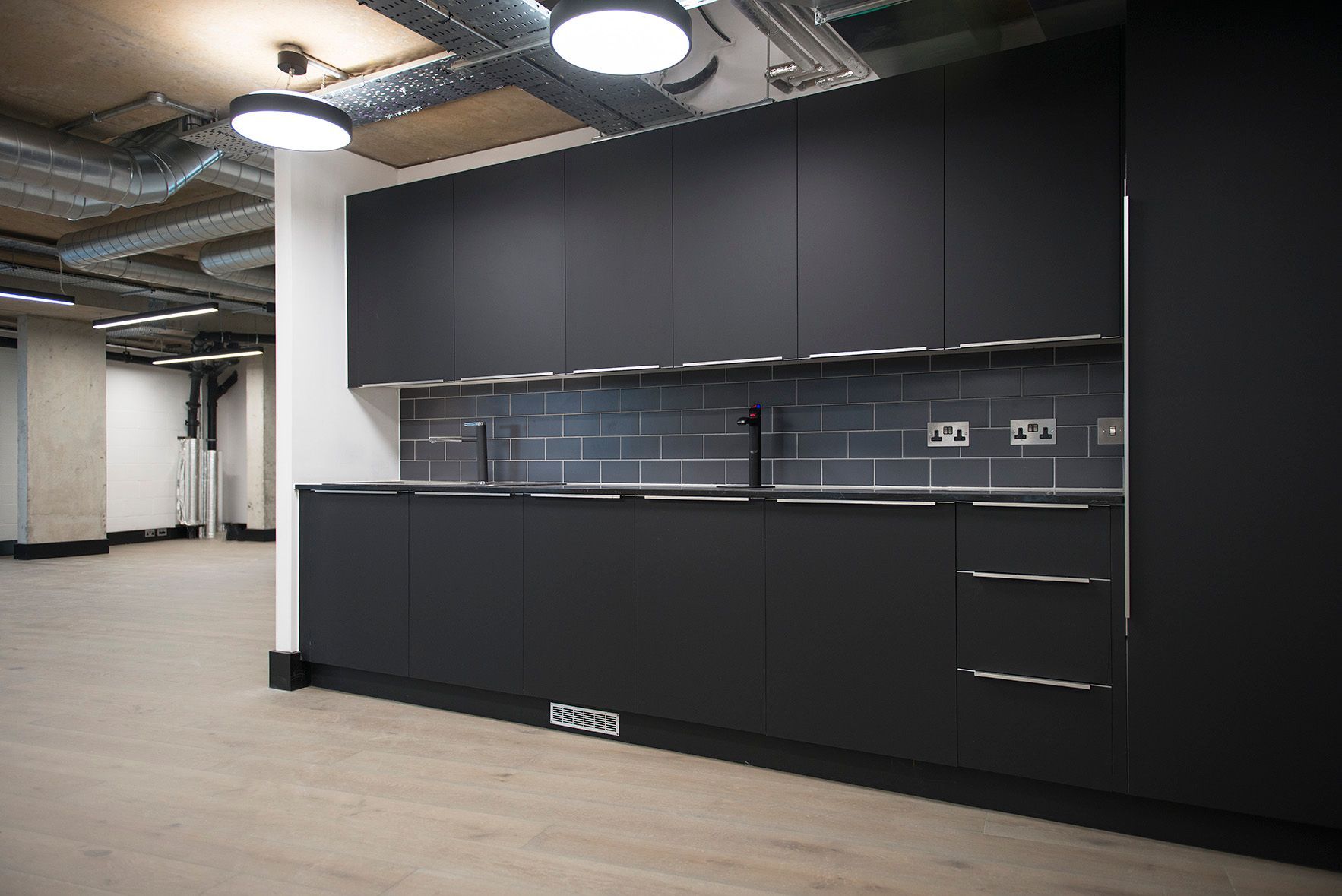 An empty kitchen with black cabinets and a sink.