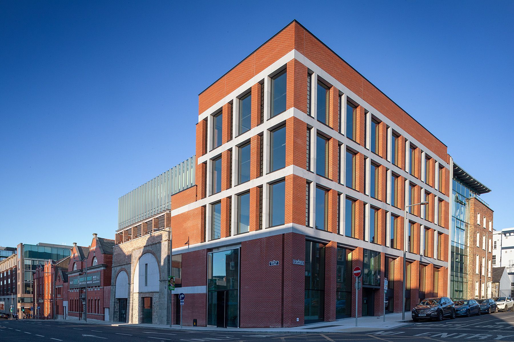 A large brick building with a lot of windows is sitting on the corner of a city street.