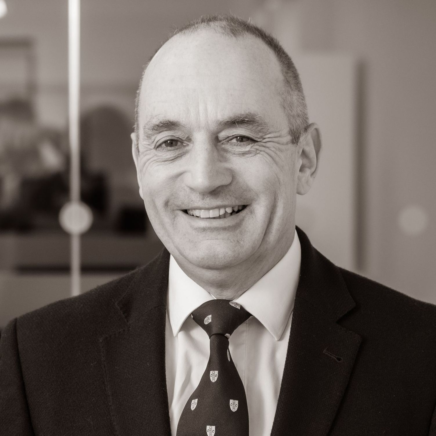 A man in a suit and tie is smiling in a black and white photo.