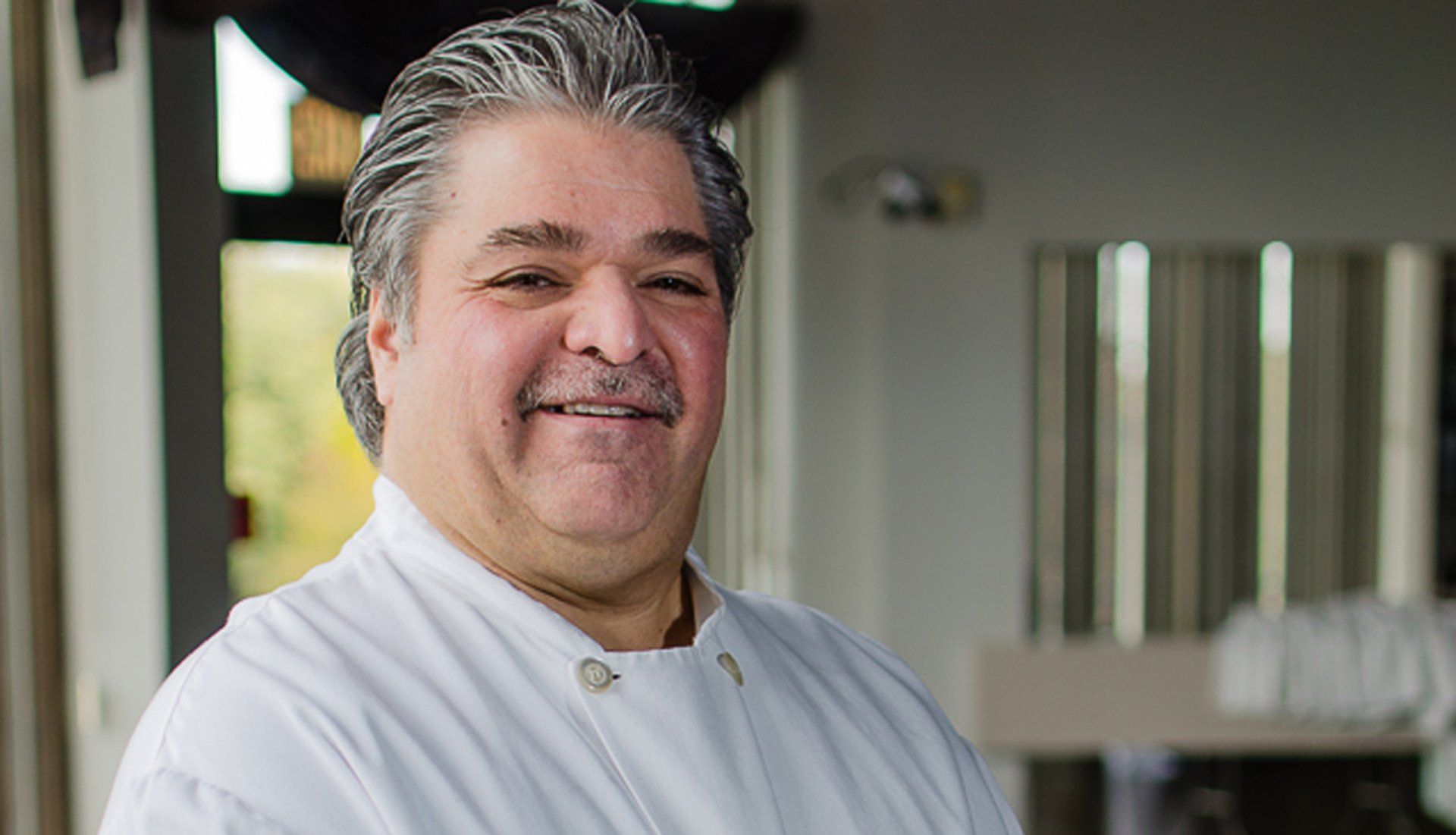 A man in a white chef 's coat is smiling for the camera.