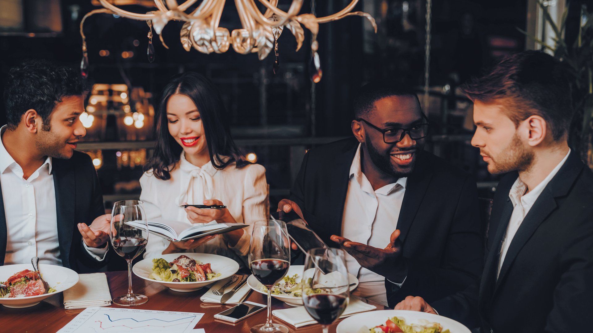 A group of people are sitting at a table in a restaurant eating food and drinking wine.