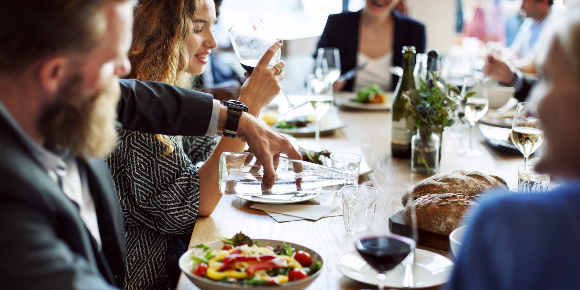 A group of people are sitting at a long table eating food and drinking wine.