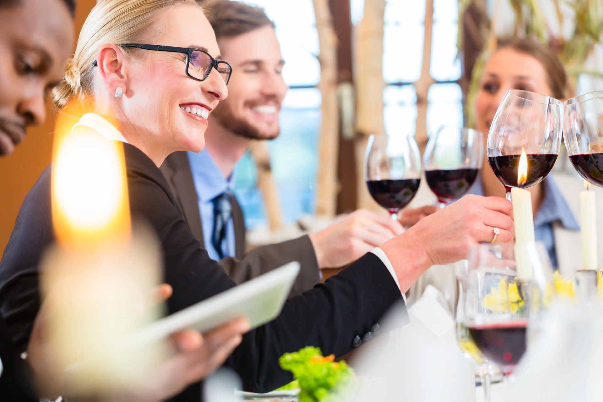 A group of people are sitting at a table with wine glasses and a tablet.