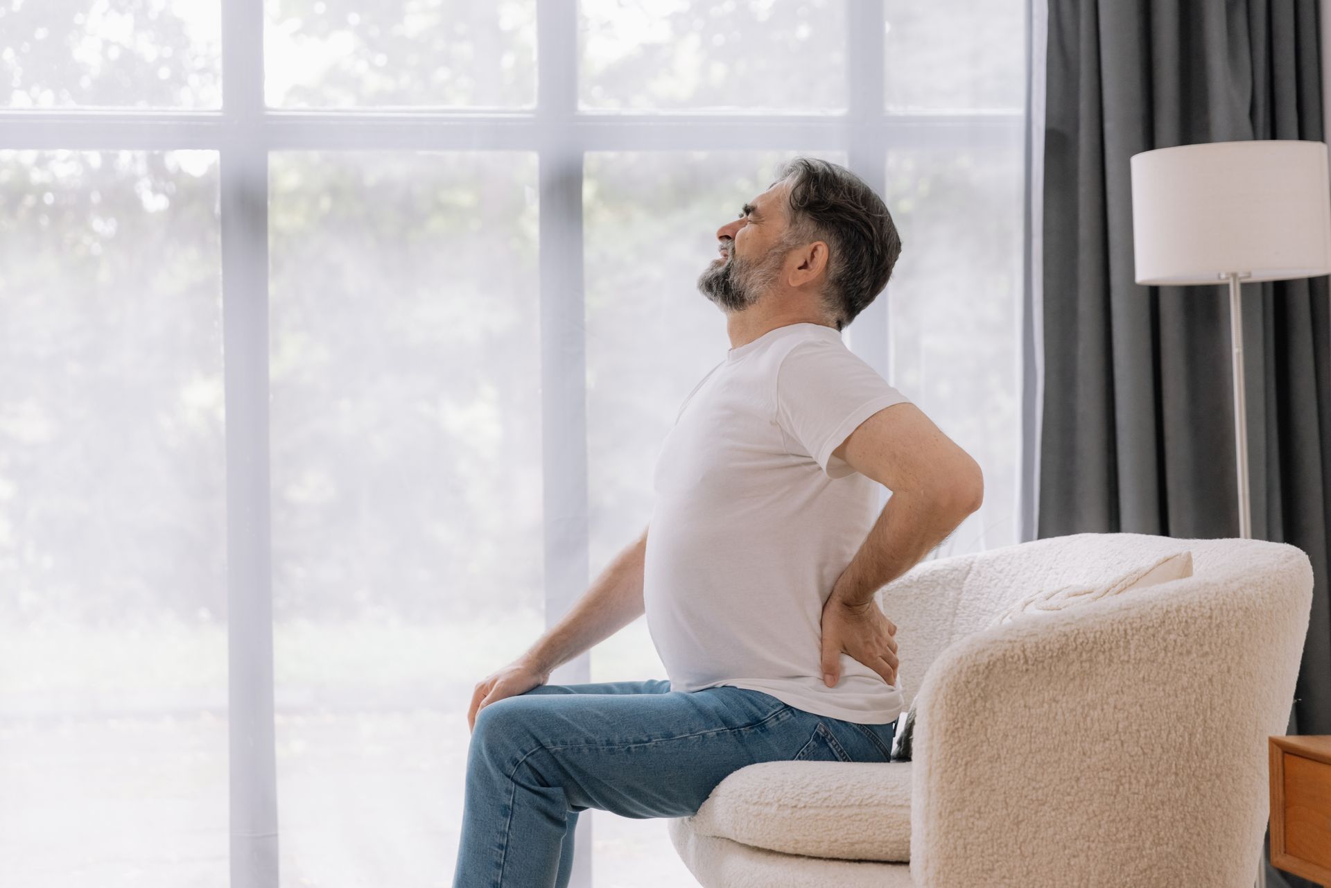 A man is sitting on a couch with his back in pain.